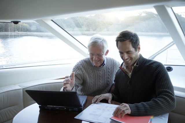 Senior and mature man sitting on yacht using laptop, smiling