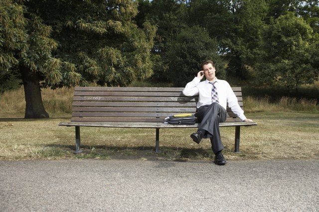 Businessman sitting on park bench, using mobile phone