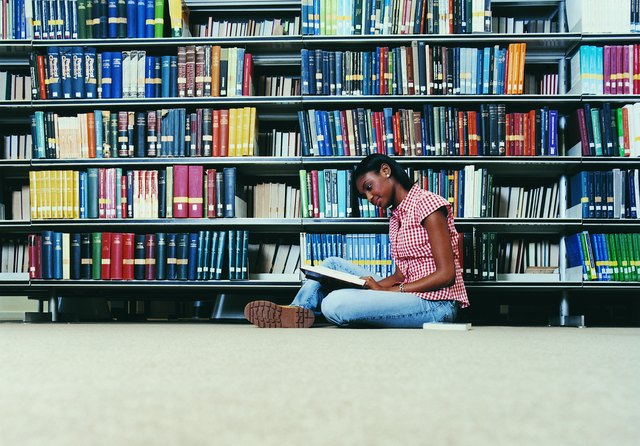Female University Student Sitting on a Library Floor Reading a Book