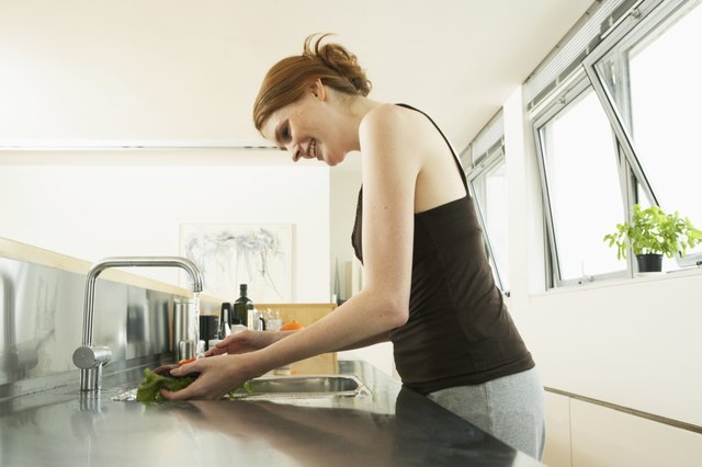 Young woman washing lettuce at kitchen sink, smiling, side view