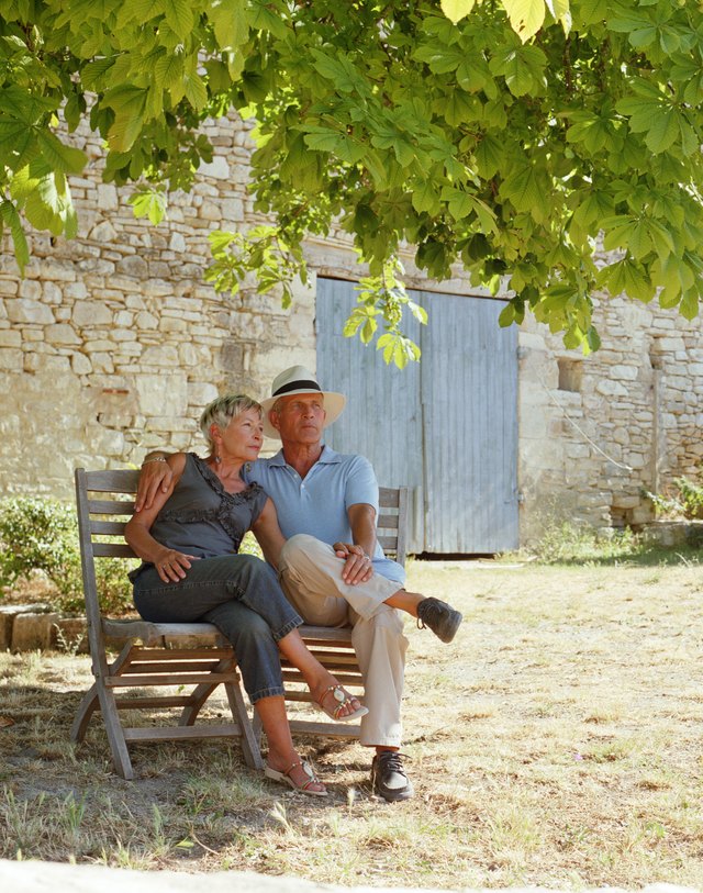 Couple embracing on chairs beneath tree by house