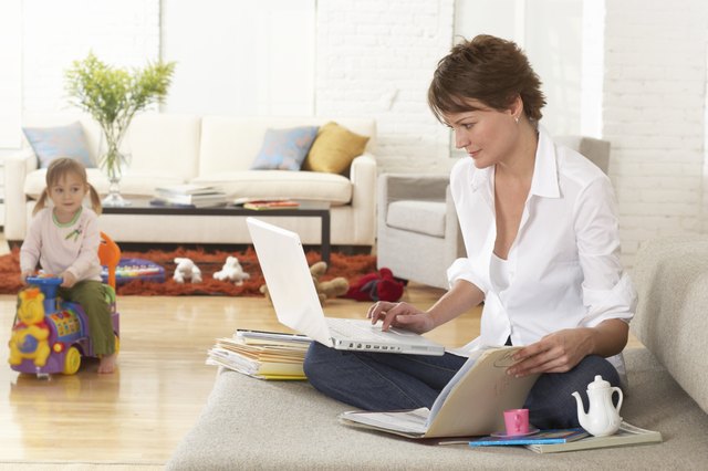 Woman using laptop on sofa, daughter (2-4) on toy in background