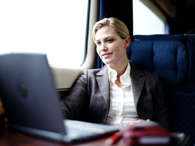 Businesswoman using laptop on train, smiling (focus on woman)