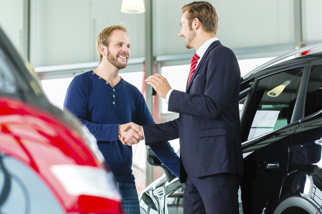 Young man and seller with auto in car dealership